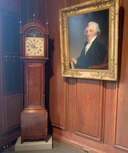 彩色照片，角落里有一个高高的箱子钟，左边墙上挂着一个男人的肖像.